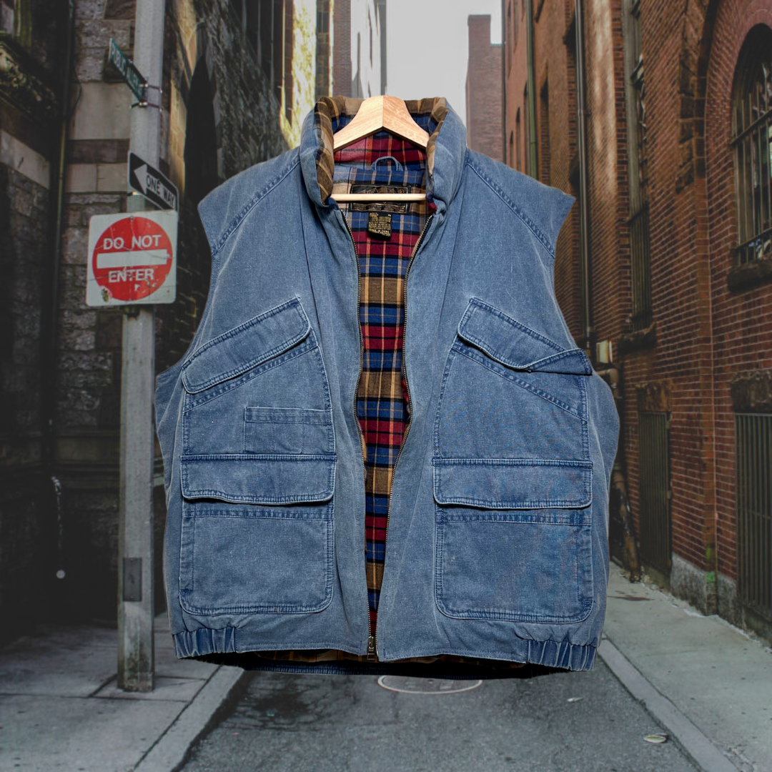Front unzipped vintage blue, zip-up, Eddie Bauer puffer vest w/ 2 chest pockets & 2 bottom pockets that fasten with Velcro. Lined with plaid cotton material. Good Kid Collective hand-picked this item.